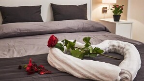 Un lit bien fait, avec une serviette blanche, une rose rouge et quelques pétales de rose.