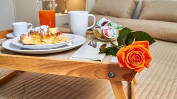 Un plateau de petit-déjeuner avec un croissant, du jus de fruits et une rose, posé sur une table en bois dans une chambre d’hôtel.