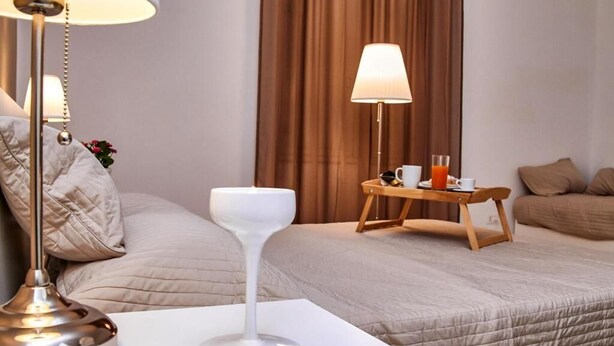 Une chambre d’hôtel avec un lit, une table de chevet avec une lampe, un plateau avec une tasse et un verre de jus d’orange, et une fenêtre avec des rideaux.