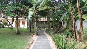 A pathway lined with pebbles and surrounded by lush greenery, leading to a building with a tiled roof and wooden doors. - Pousada Ubajara (Ubajara)
