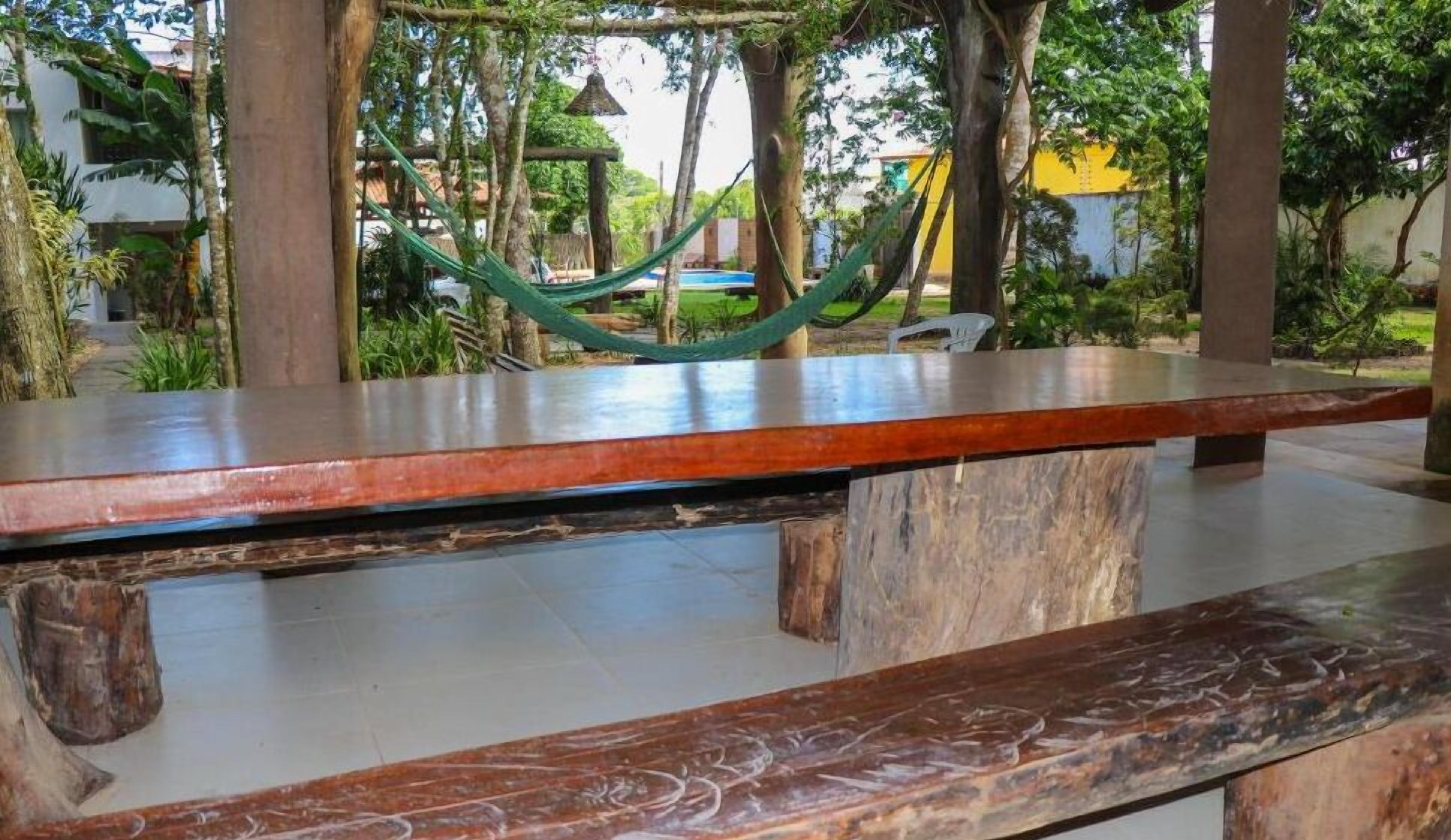 A wooden bench with a marble top in a garden area with trees and a hammock.