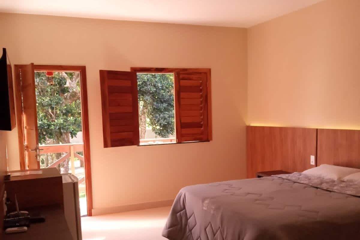 A bedroom with a bed, a desk, and two windows with wooden shutters.