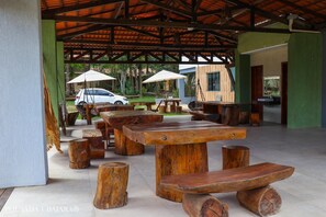 An outdoor patio with wooden tables and benches, a covered area with a roof, and a car parked in the background. - Pousada Ubajara (Ubajara)