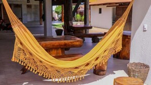 A hammock tied between wooden posts, a wooden table, and a small stool in an outdoor setting with a tiled floor and a white wall. - Pousada Ubajara (Ubajara)