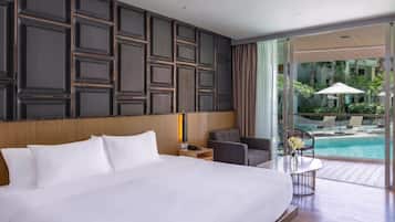 A hotel room with a large bed, a desk, a chair, a small table with flowers, and a view of a swimming pool.