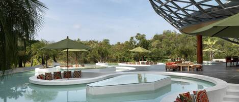 A pool area with seating and umbrellas, surrounded by lush greenery.