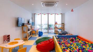 A children's playroom with a ball pit, seating areas, and a television.