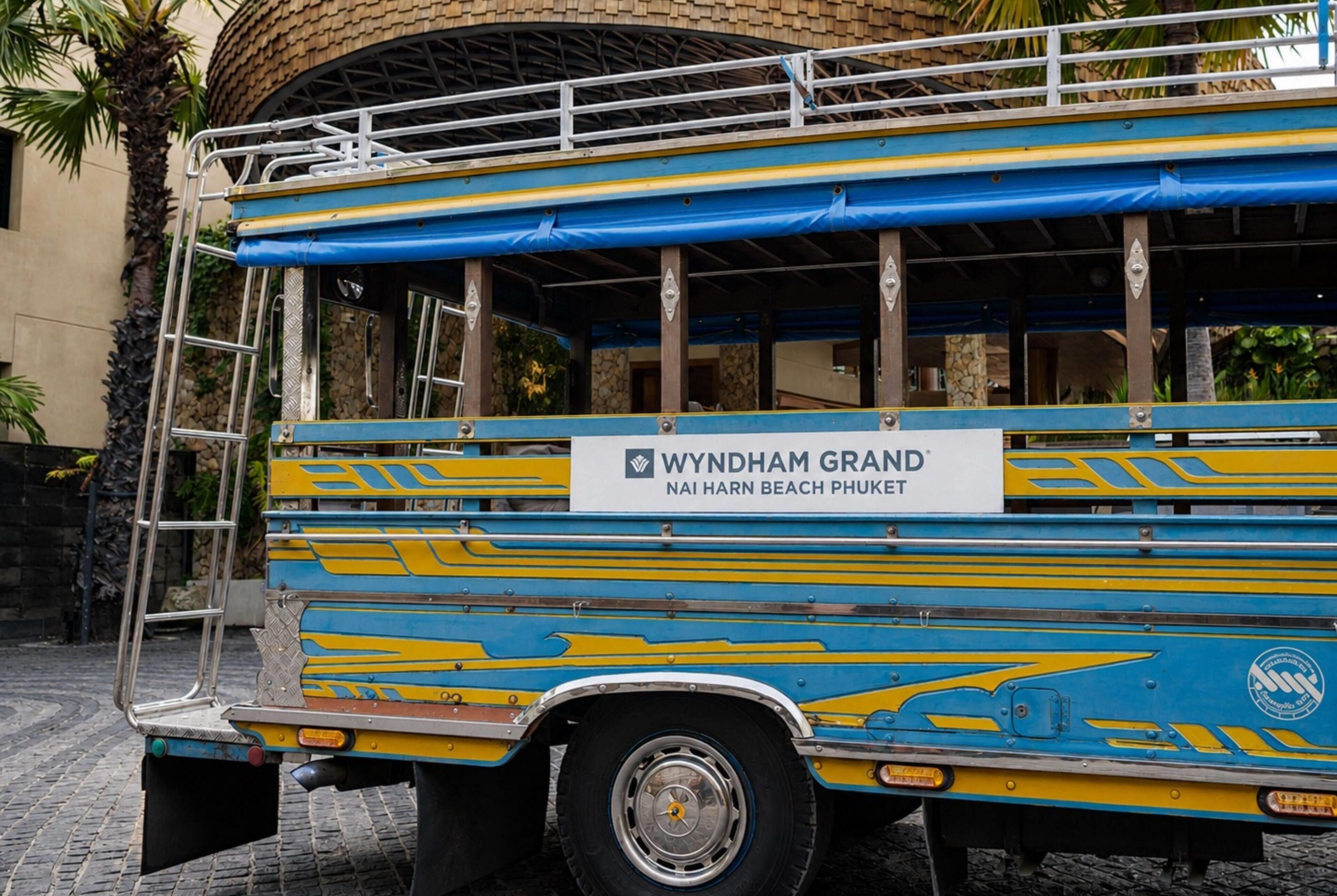 A colorful bus with 'WYNDHAM GRAND NAI HARN BEACH PHUKET' written on the side.
