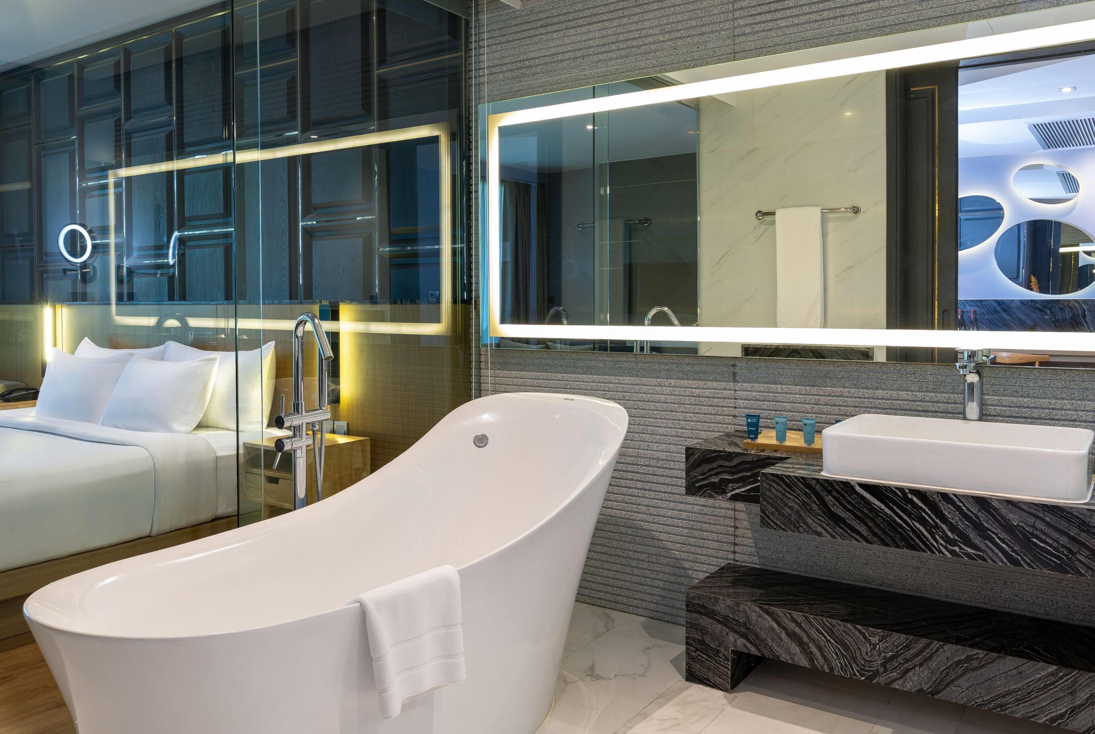 Un baño moderno con una bañera independiente, un espejo grande y un tocador con encimera de mármol.