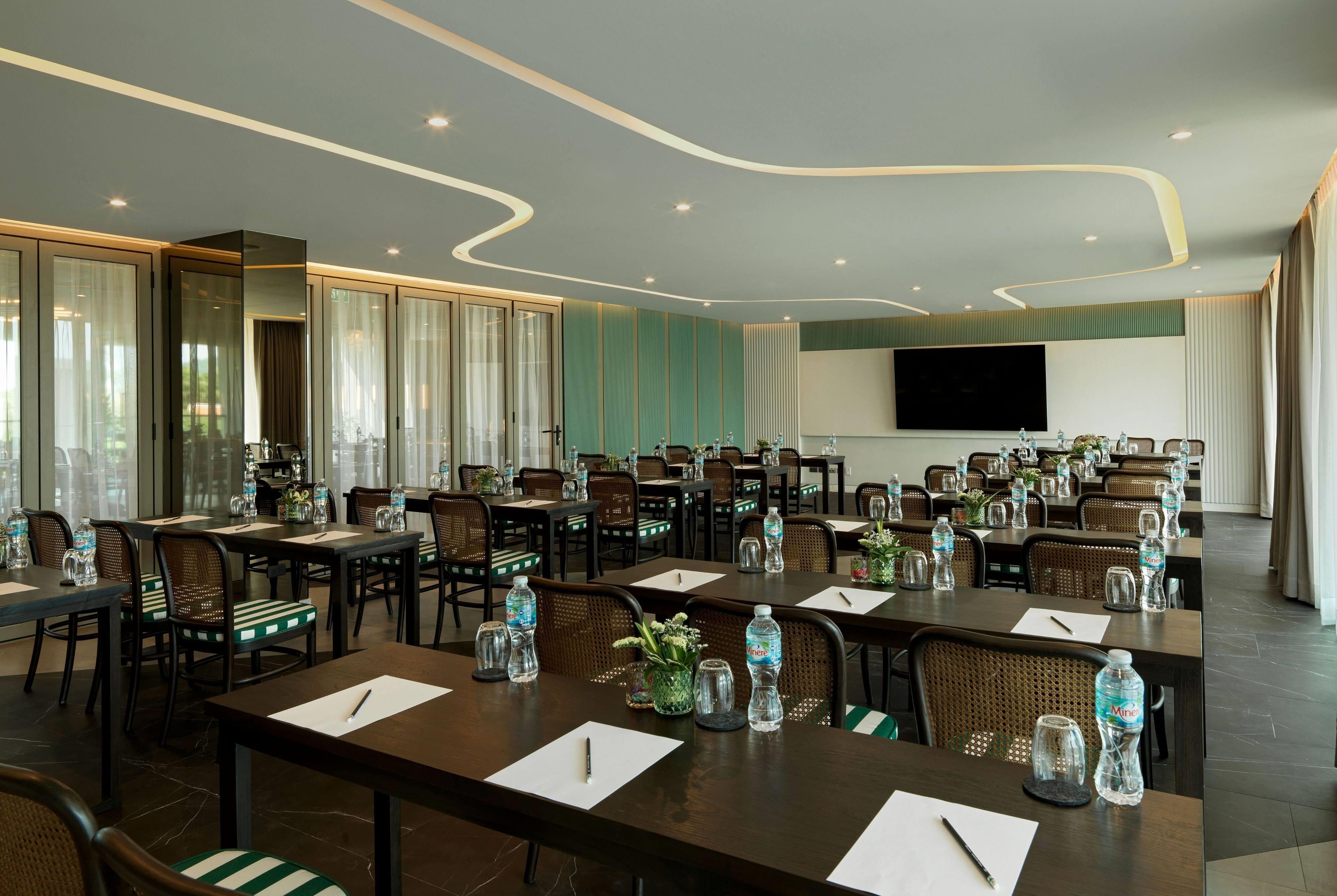 A conference room with multiple tables, chairs, and a large screen.