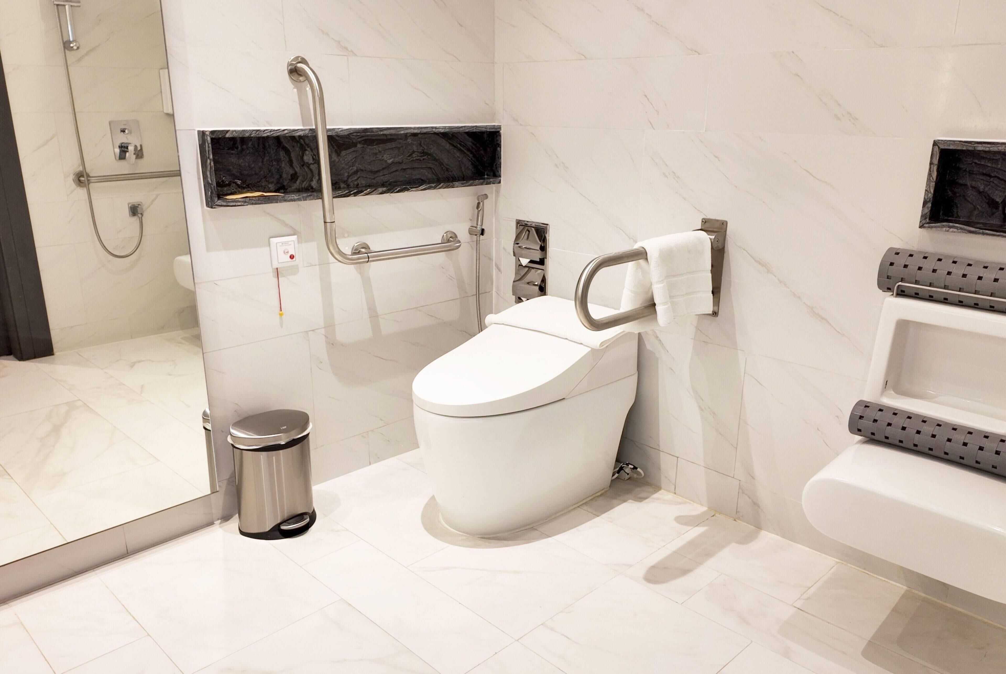 A modern bathroom with a toilet, bidet, handrail, and a trash bin.