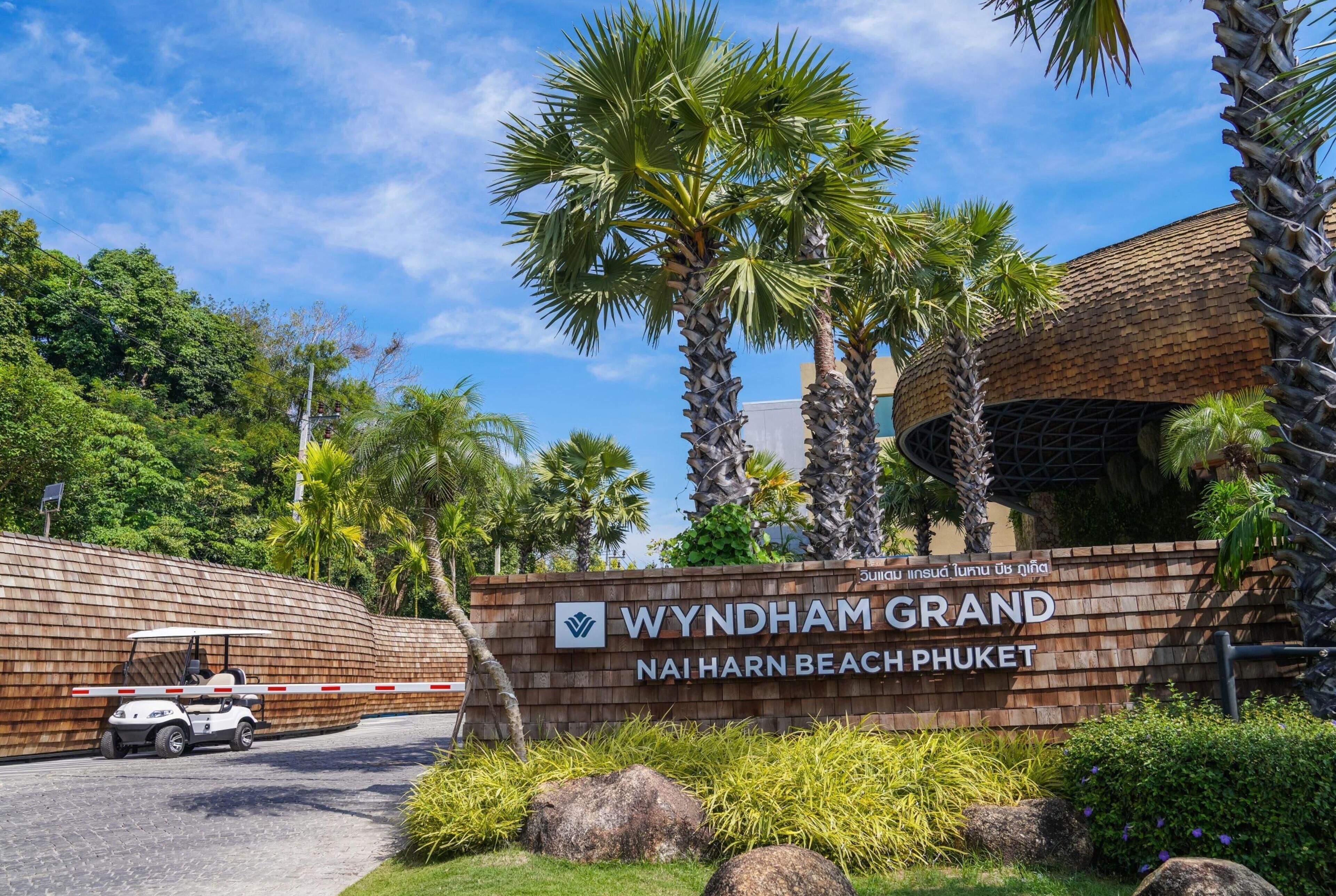 Letrero del Wyndham Grand NAI HARN BEACH PHUKET con palmeras y un muro de ladrillo.