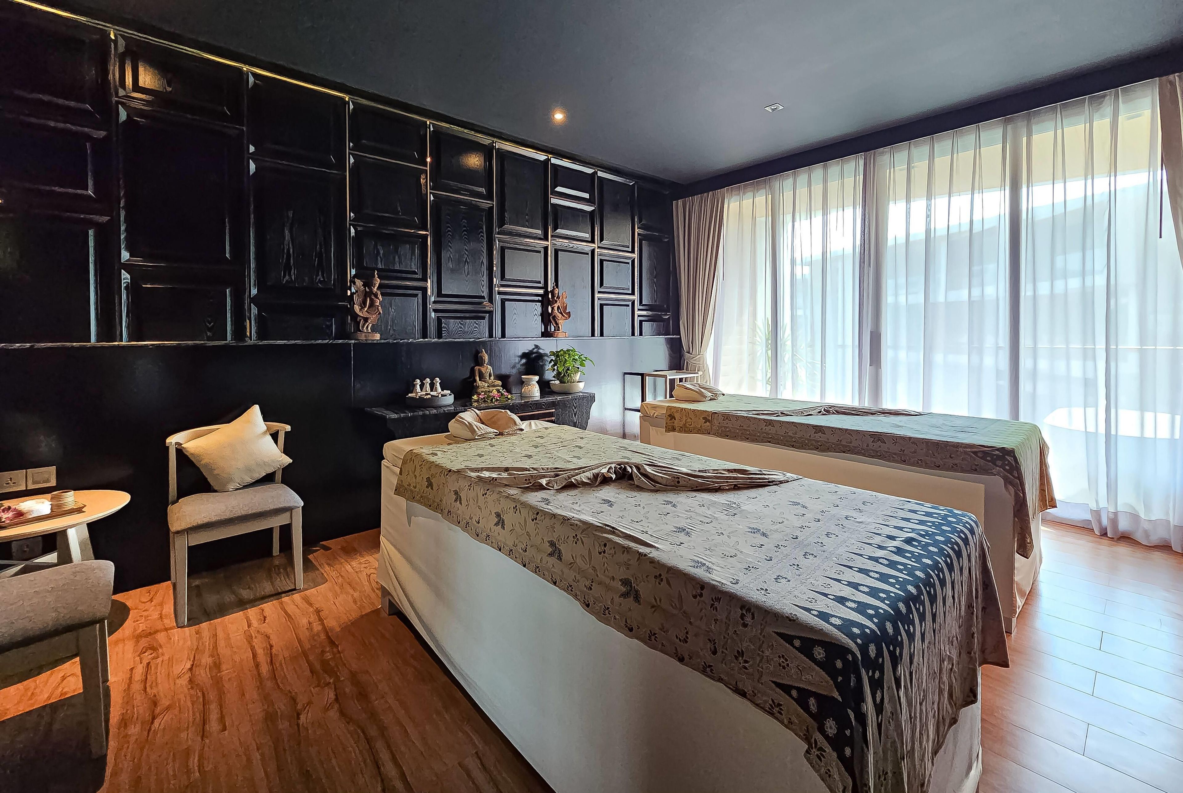 Habitación de hotel con dos camas, una mesita, una silla y una ventana con cortinas traslúcidas.