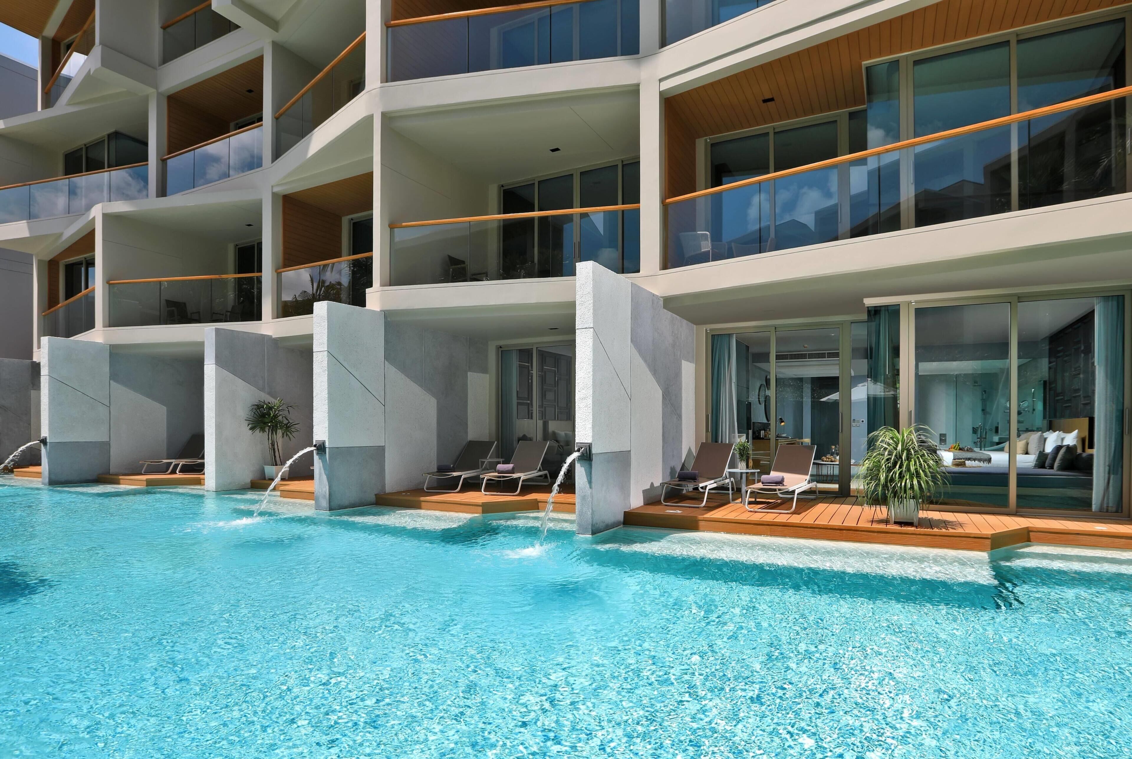 A modern hotel with a pool, multiple balconies, and sun loungers.
