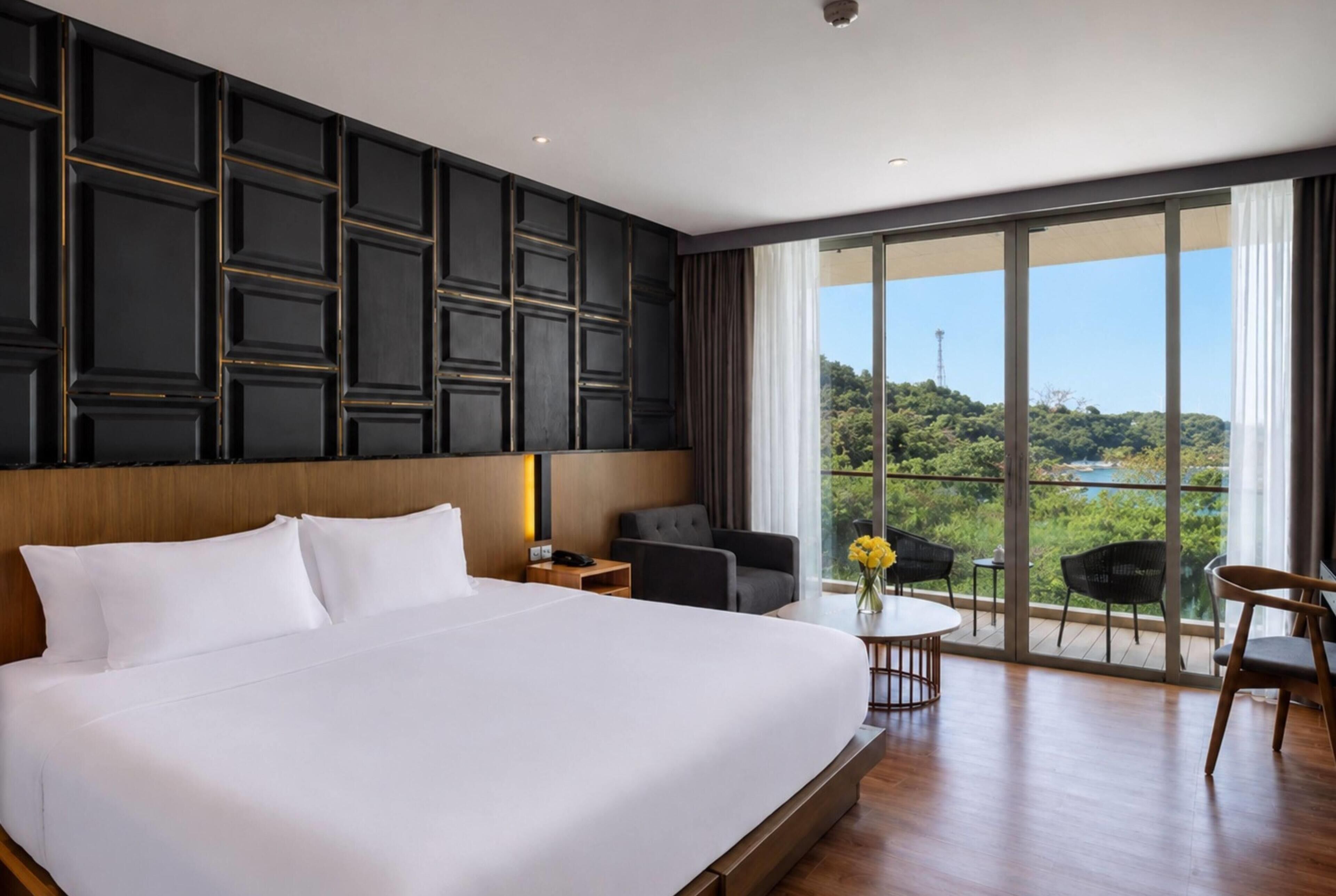 A hotel room with a large bed, a desk, a chair, and a view of a natural landscape.