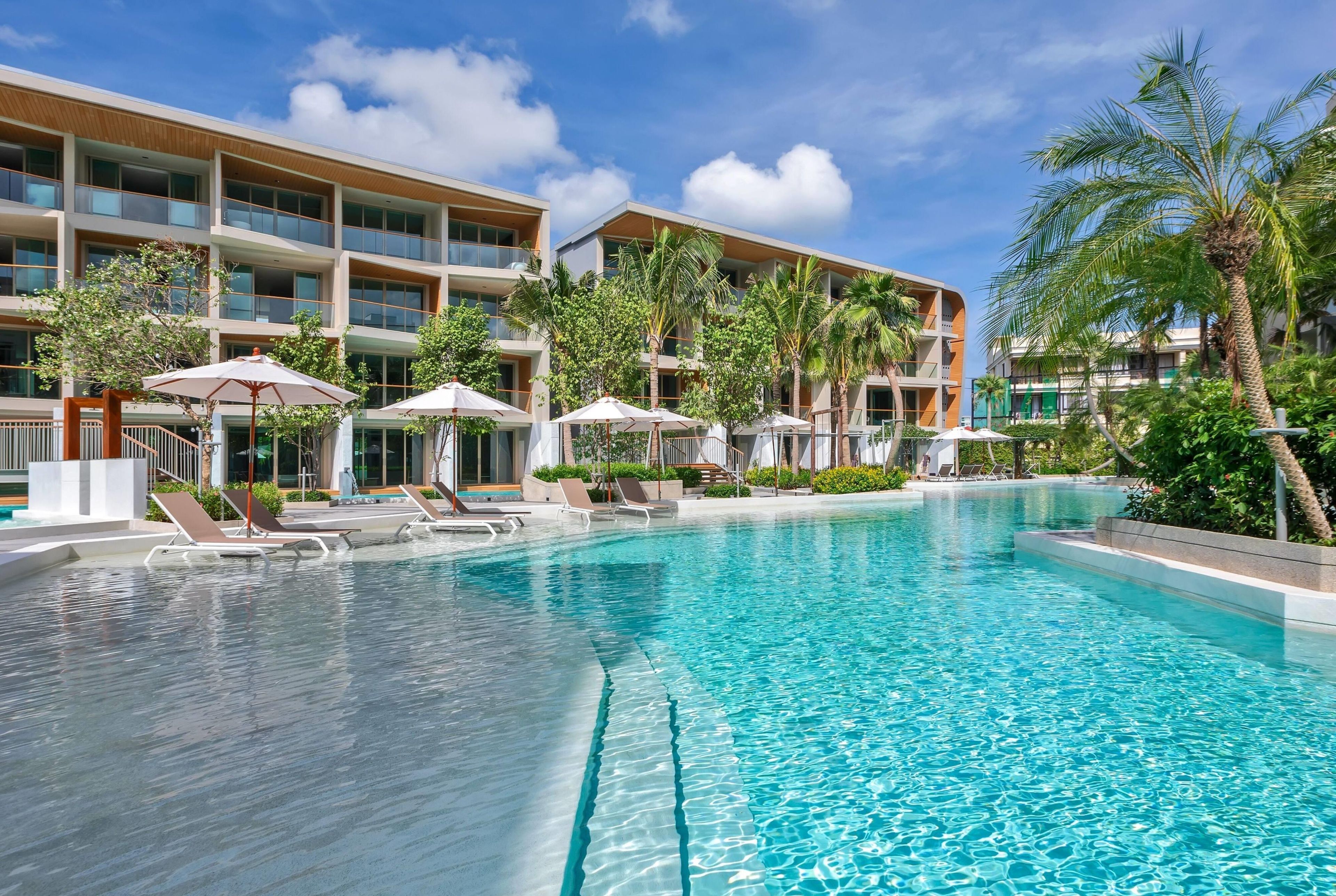A hotel with a swimming pool, multiple balconies, and palm trees.