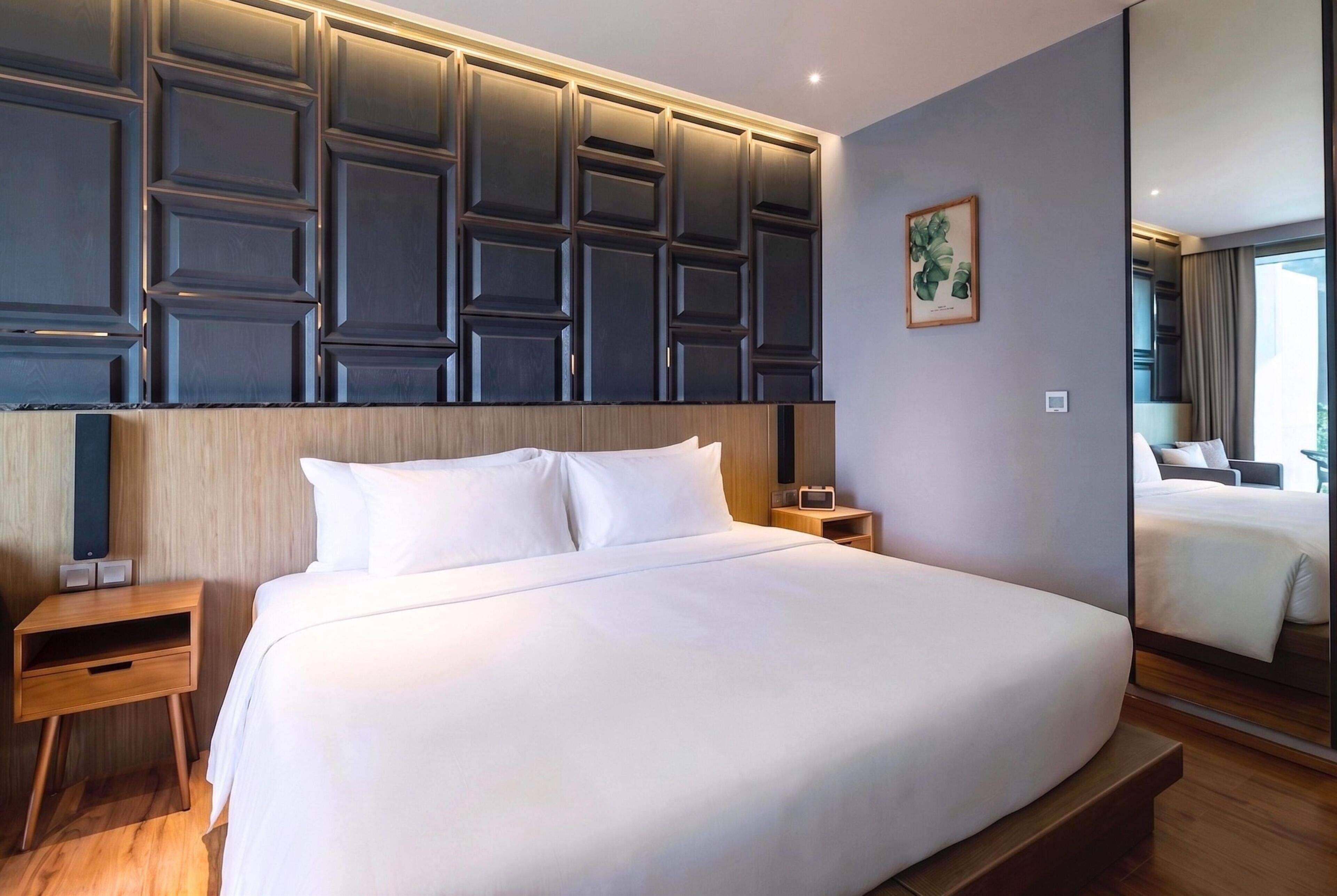A hotel room with a large bed, wooden headboard, bedside tables, and a mirror.