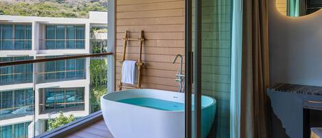 Un baño moderno con una bañera independiente, ducha con cerramiento de vidrio y vistas a un edificio con múltiples ventanas.