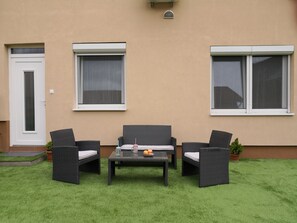 A patio with a sofa, two chairs, and a table. There are two windows and a door. - Green Garden Plus Apartman (Budapest)