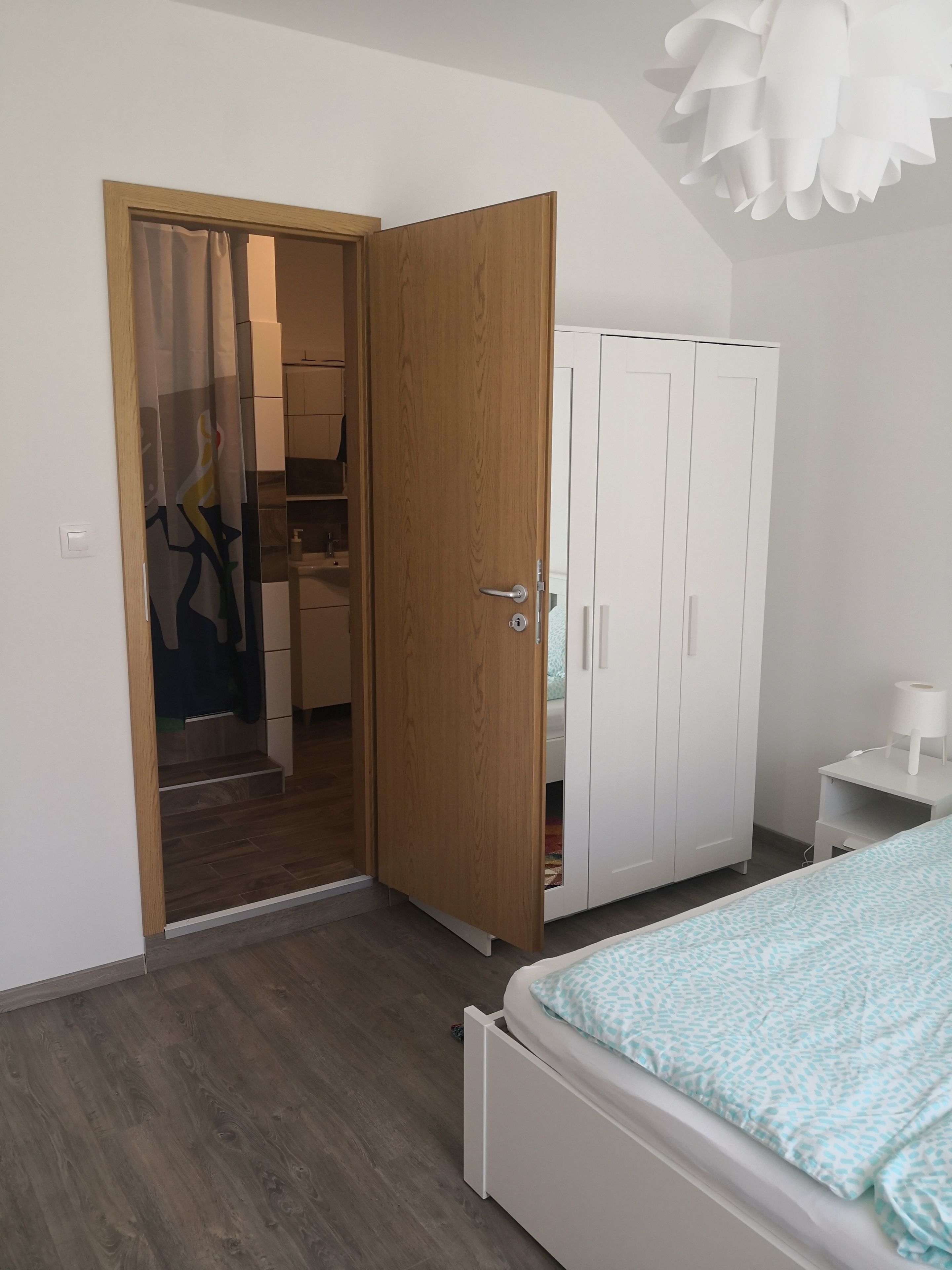 Quarto com cama, guarda-roupa e banheiro visível por uma porta aberta.