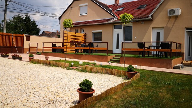 A two-story house with a red-tiled roof, a balcony with outdoor furniture, and a gravel driveway. - Green Garden Plus Apartman (Budapest)