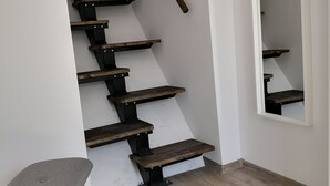 A staircase with wooden steps and black metal railings, a grey chair, and a grey rug on a wooden floor. - Green Garden Plus Apartman (Budapest)