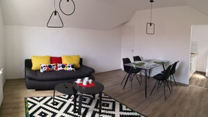 A modern living room with a black sofa, colorful cushions, a dining table with chairs, and a patterned rug. - Green Garden Plus Apartman (Budapest)