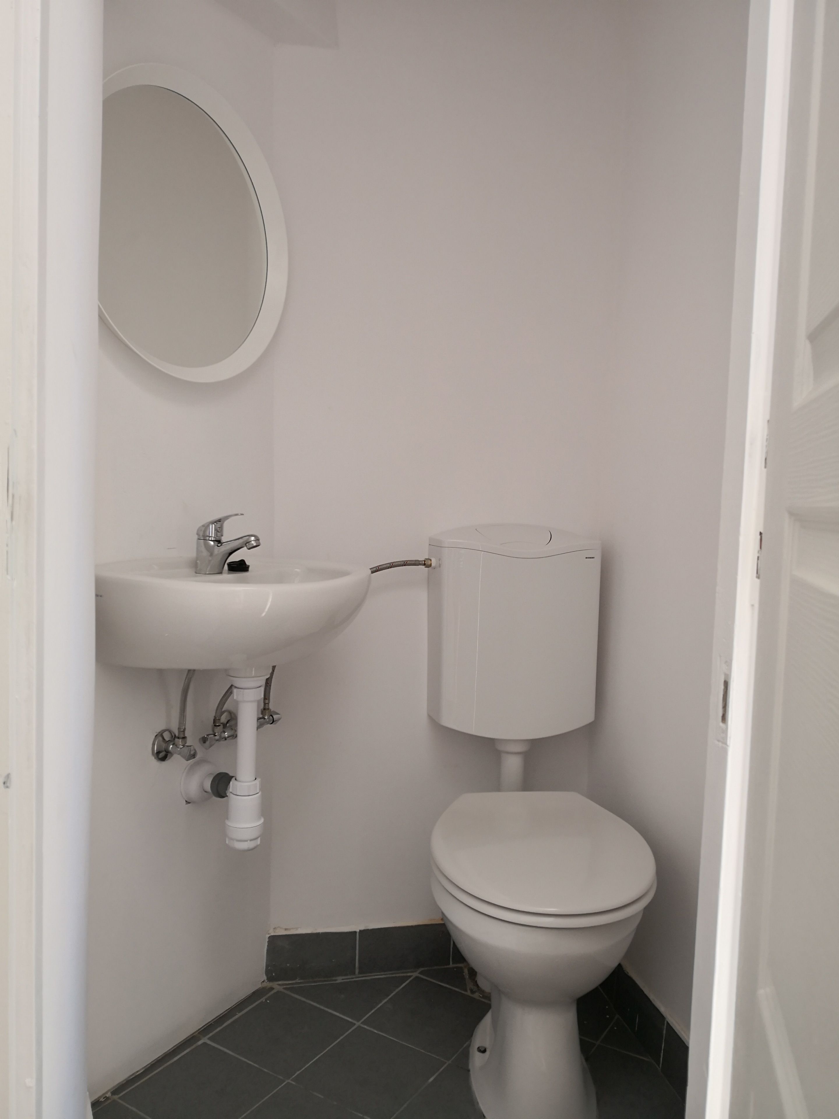 Un baño pequeño y limpio con lavamanos, inodoro y espejo blancos.