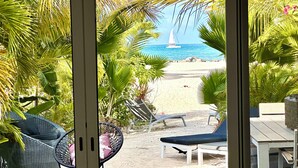 Blick auf einen Strand von einer überdachten Terrasse mit Liegestühlen und einer Rattansofa.