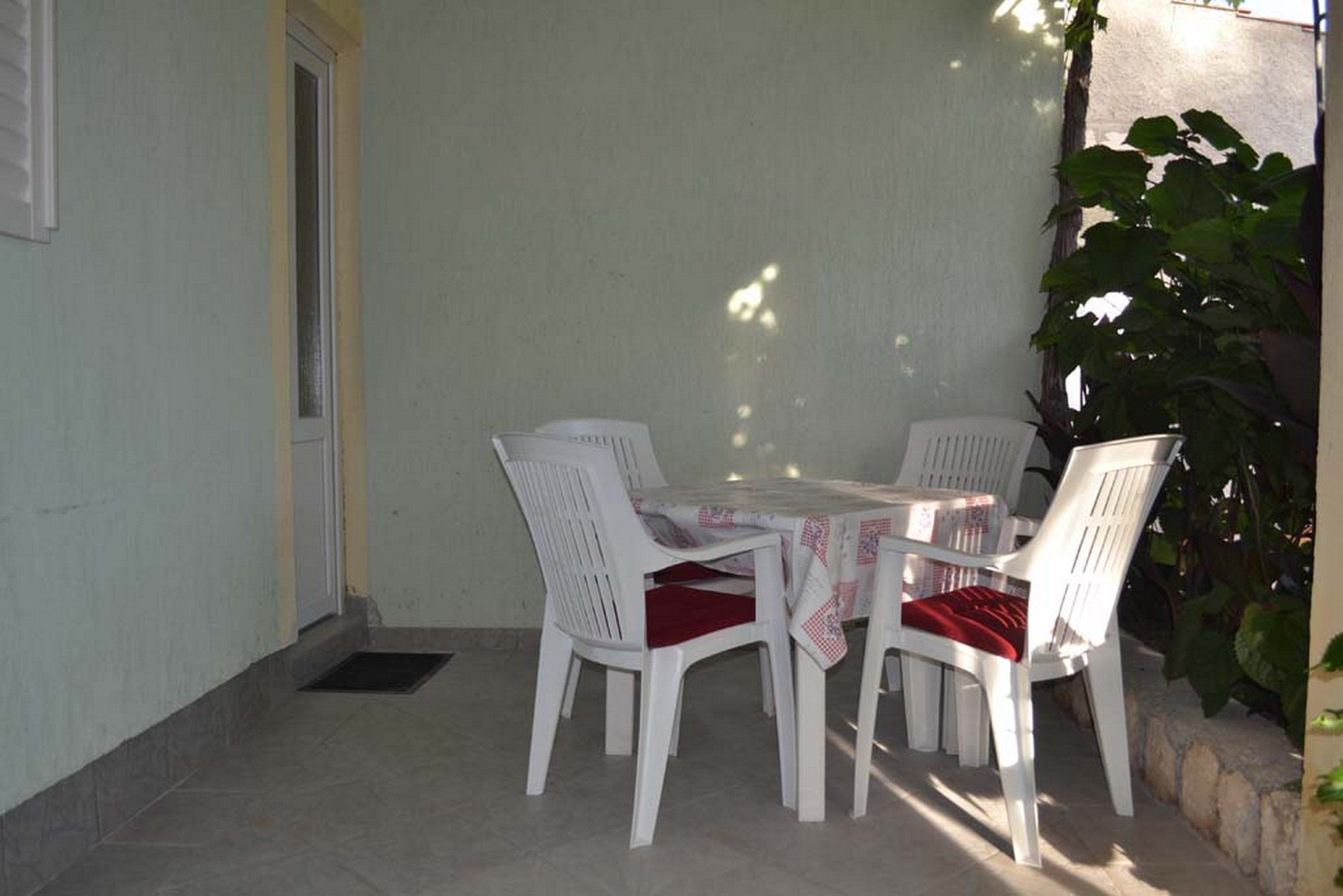 A patio with a table and four white chairs, a door, and a potted plant.