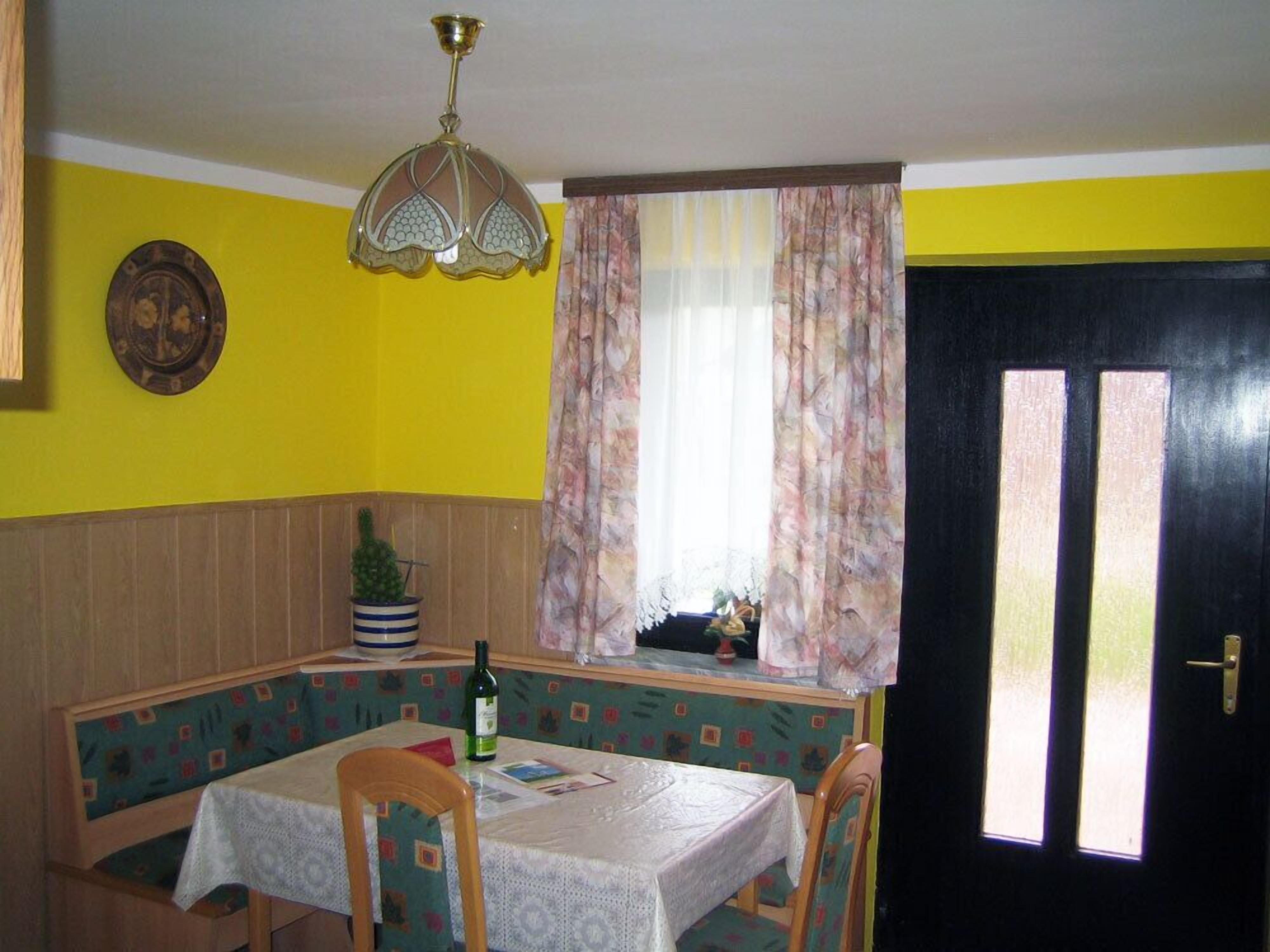 A dining area with a table set for two, a decorative ceiling light, a window with curtains, and a door with glass panels.