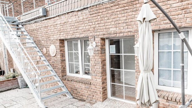 Un edificio de ladrillo con una escalera metálica, ventanas grandes y un paraguas blanco.