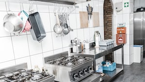 Una cocina comercial con electrodomésticos de acero inoxidable, utensilios colgando y una pared de ladrillo.