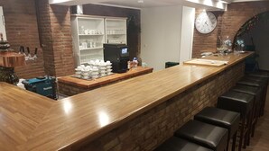 Una zona de bar con mostrador de madera, una máquina de café y un reloj en la pared.