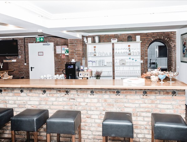 Zona de bar con pared de ladrillo, taburetes, estanterías con vasos y una máquina de café.