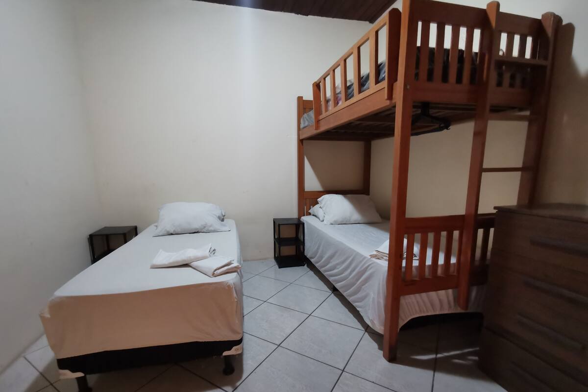 Un dormitorio con dos literas, una mesita de noche pequeña, un aparador y piso de baldosas.