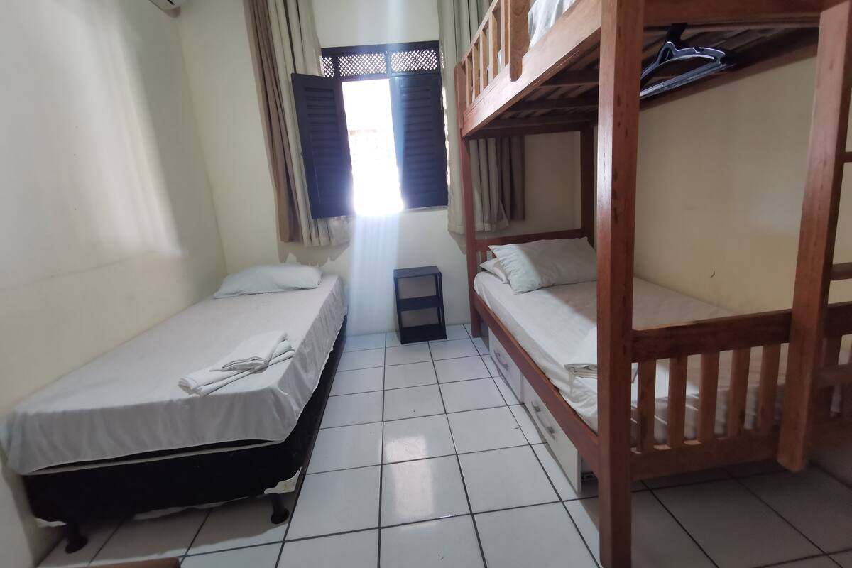 Una habitación con dos literas, una mesita pequeña y un ventanal con cortinas.
