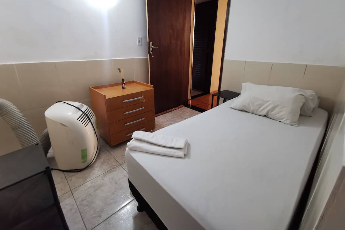 Una habitación de hotel con una cama, un aparador de madera, un calentador blanco y una puerta que da a otra habitación.
