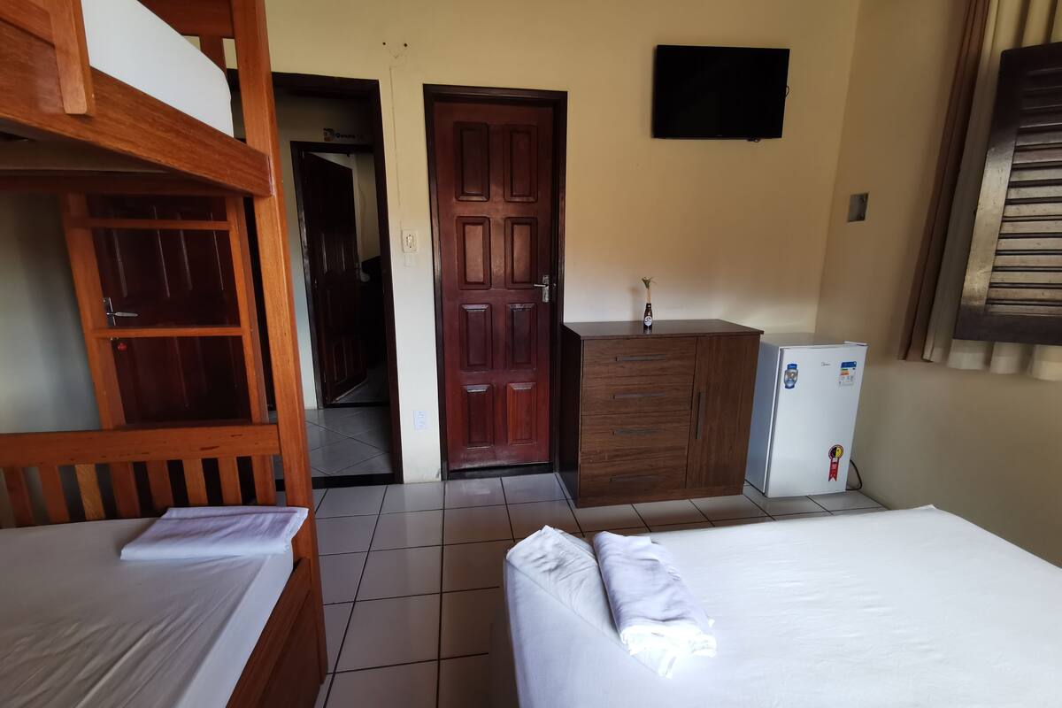Una habitación con dos literas, un armario de madera, un refrigerador pequeño y una puerta que da a otra habitación.