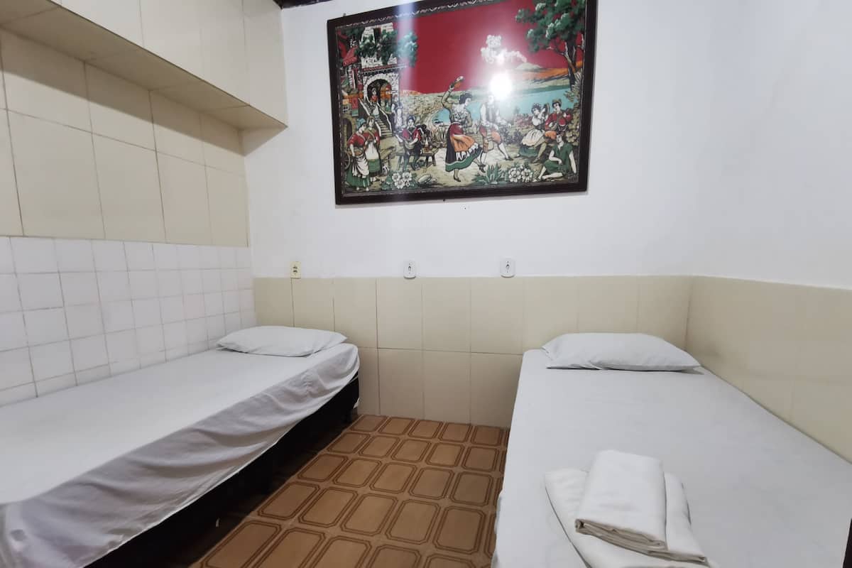 Una habitación pequeña y limpia con dos camas individuales, piso de baldosas y un cuadro colgado en la pared.