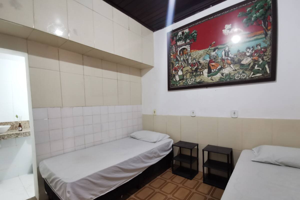 Una habitación pequeña y ordenada con una cama individual, una mesita y un cuadro colgado en la pared.