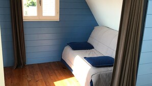 A bedroom with a sloped ceiling, a window, a bed, and curtains.