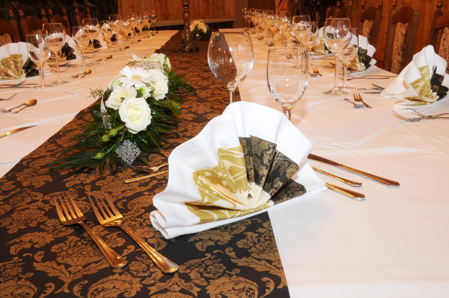 A banquet table set with gold cutlery, white napkins, and a floral centerpiece.