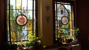Una habitación con dos ventanas grandes que presentan vidrieras, un radiador y varias plantas en macetas.