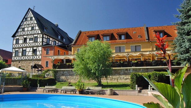 Un edificio de estilo europeo tradicional con piscina, bancos y plantas en macetas.