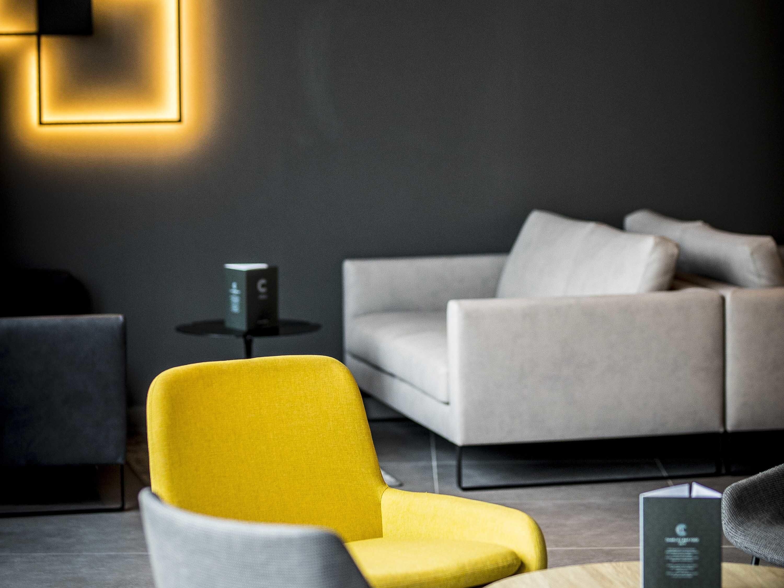 Una habitación moderna con un sillón amarillo, un sofá gris y una pequeña mesa con un dispositivo.