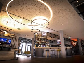 A modern bar area with a circular light fixture, a bar counter, and stools. - Ibis Wels (Wels)