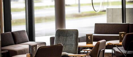 Interior de una cafetería moderna con mesas, sillas y vistas a la calle.