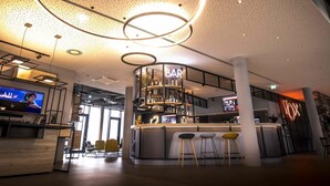 A modern bar area with a circular light fixture, a bar counter, and stools. - Ibis Wels (Wels)