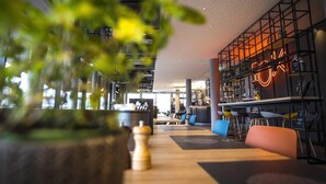 A modern interior with a bar area, seating, and a large plant in the foreground. - Ibis Wels (Wels)